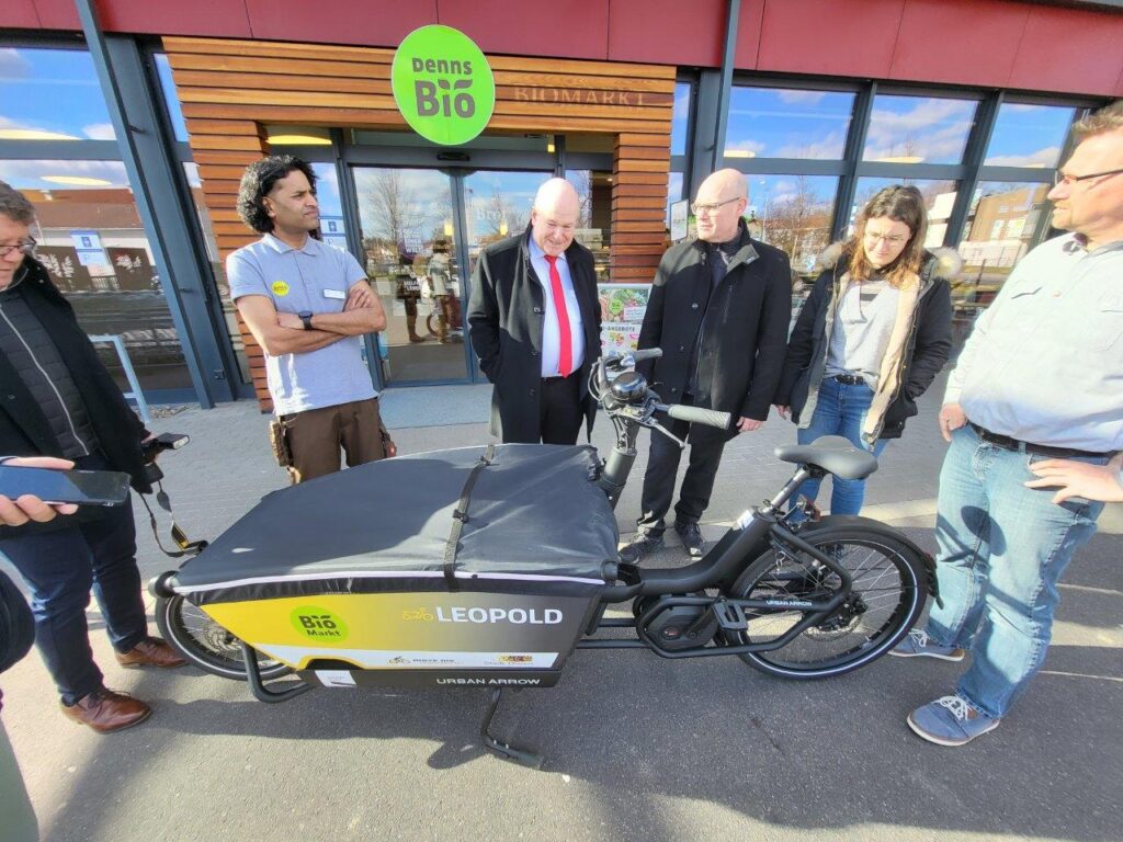 Mehrere Personen stehen am Biomarkt Denns vor einem Lastenrad