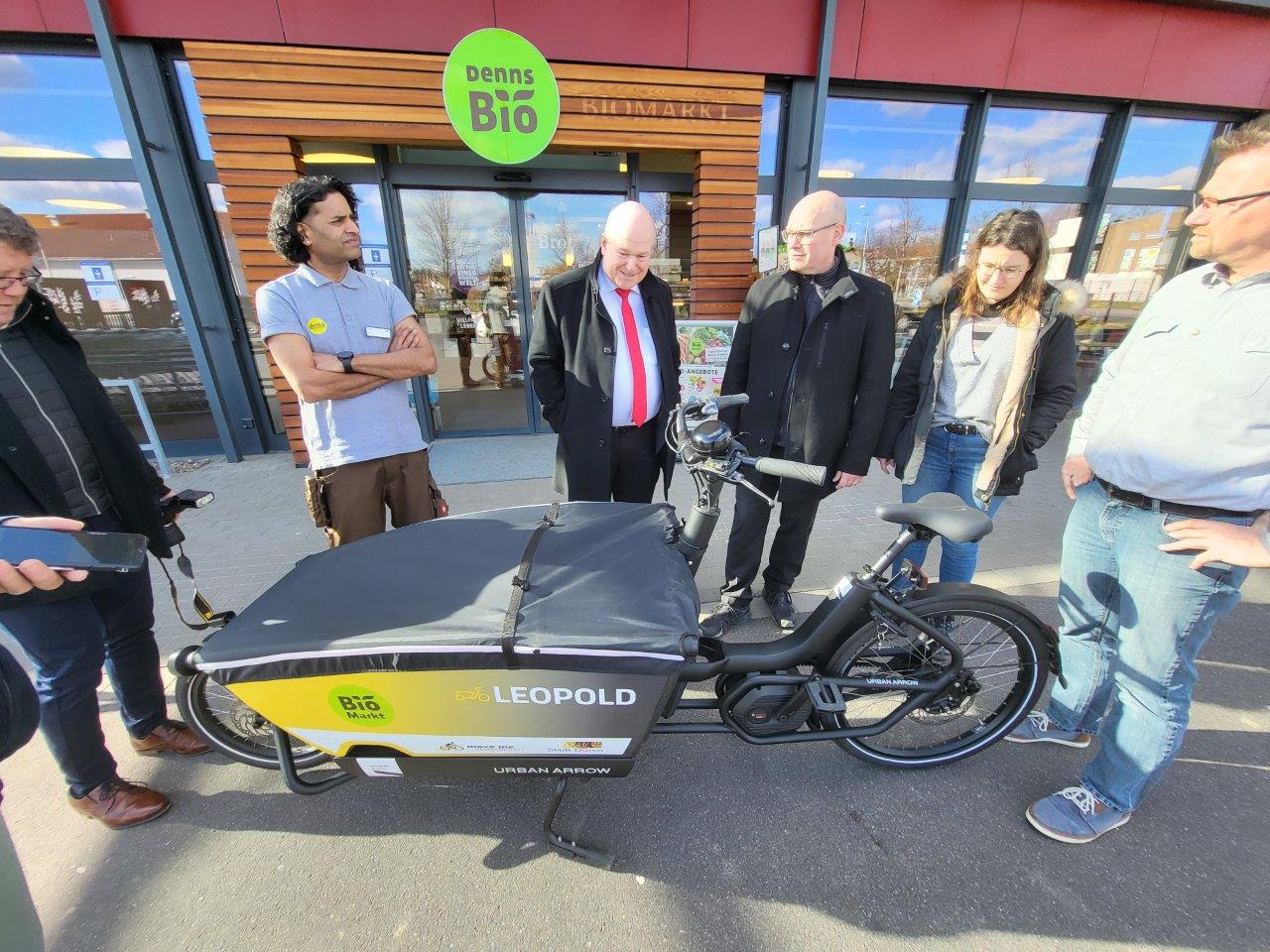 Mehrere Personen stehen am Biomarkt Denns vor einem Lastenrad